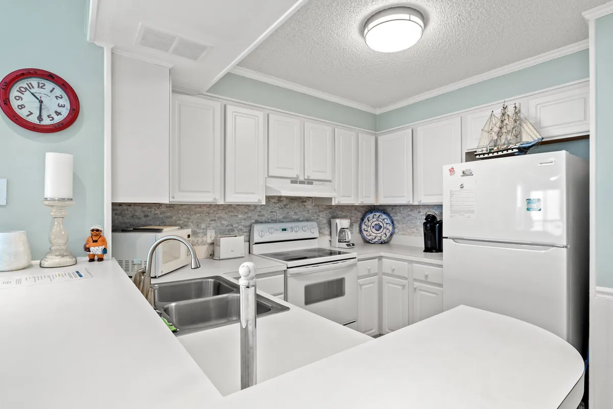 Featuring a bright, well-equipped kitchen with white cabinetry, stainless steel appliances, a decorative plate, a ship model, and a kitchen island, this cheerful space is designed for cooking, entertaining, and family meals. The layout encourages conversation and the creation of shared memories.