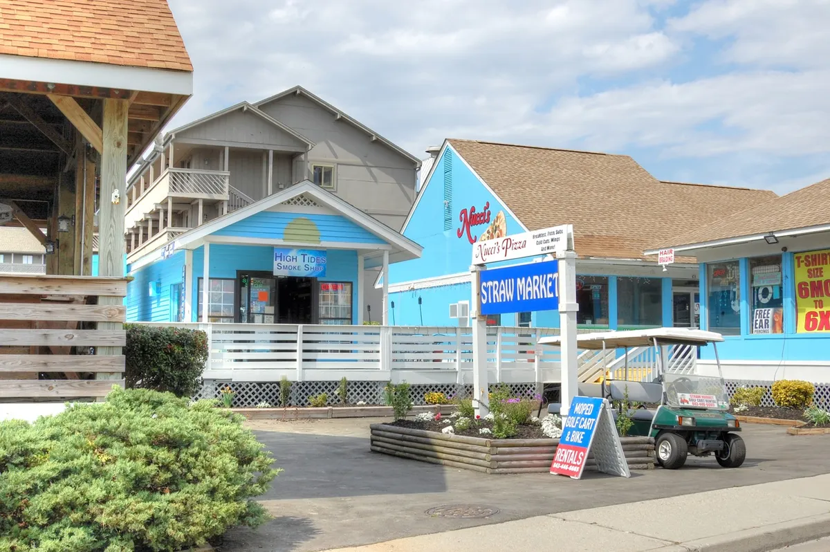A cheerful exterior scene highlighting colorful building facades, signage for the Straw Market and High Tide Smoke Shop, and a parked golf cart. The inviting environment suggests opportunities for shopping, casual exploration, and enjoying the local flavor.
