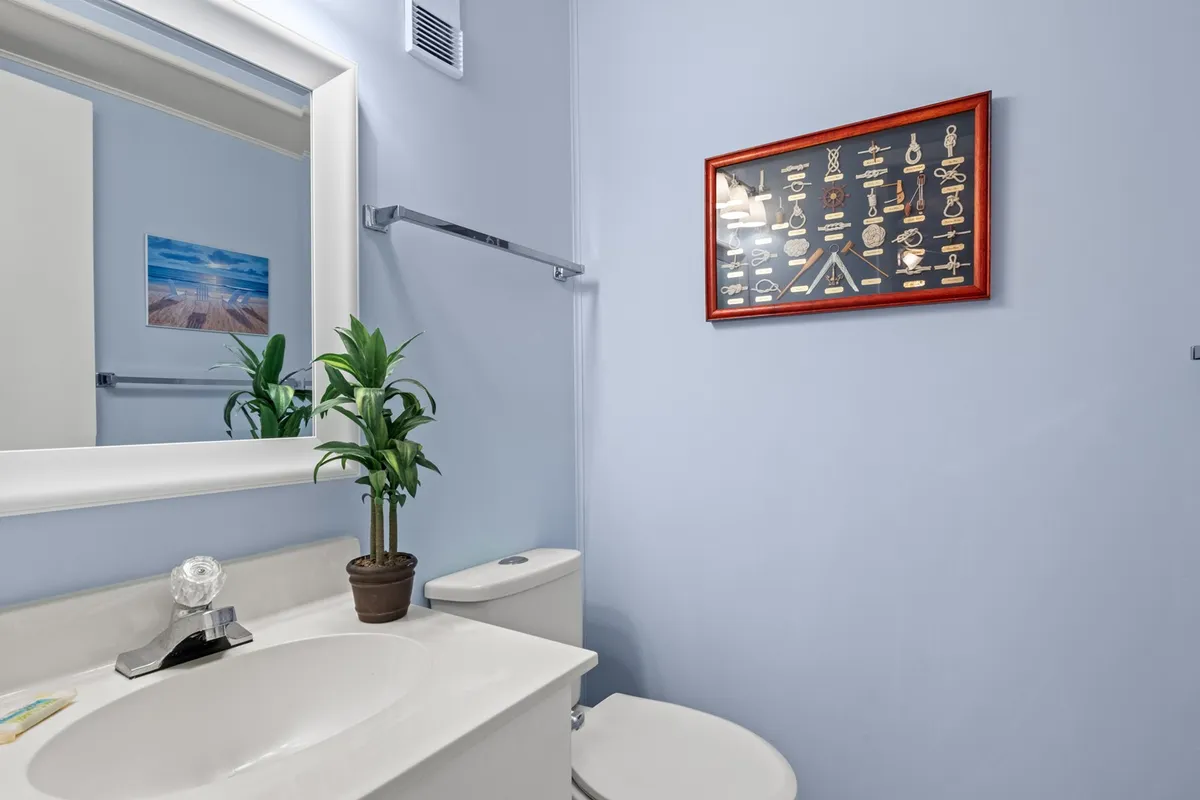 A calm, inviting bathroom scene with a mirror, sink, framed artwork, and a touch of greenery. The setup is ideal for morning rituals and relaxing self-care routines after a day at the beach.